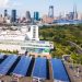 Solar carport canopies over a parking lot with a city skyline behind